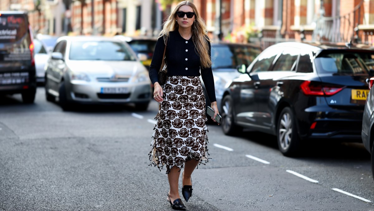LONDON, ENGLAND - SEPTEMBER 18: A guest is seen wearing a black fitted knit cardigan with white buttons; a cream midi skirt with an allover dark brown floral print and decorative knotted trim at the hem from Essentiel Antwerp; black leather loafers with woven detailing; a brown Louis Vuitton Monogram Pochette shoulder bag; small earrings and rings; black rectangular sunglasses; long blonde hair worn loose outside the Bora Aksu show during London Fashion Week September 2026 on September 18, 2026 in London, England. (Photo by Moritz Scholz/Getty Images)