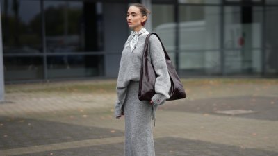 DUESSELDORF, GERMANY - OCTOBER 14: Evi Wave is seen wearing an oversized boatneck grey pullover by Aylin Koenig x Anita Hass with a slouchy fit, dropped shoulders and elongated sleeves made of a soft alpaca mix, it features an embroidered red heart one cuff; a full-length tube grey skirt by Aylin Koenig x Anita Hass in matching soft alpaca mix, with straight silhouette with a slightly flared hemline forming a co-ord set with the top; under the top she layered a white crewneck t-shirt; she carries an oversized shoulder hobo bag by Arket in high-shine patent leather in burgundy with a slouchy body; a pair of pointed-toe beige slingback kitten heels in monogram canvas by Gucci, featuring a brown logo-jacquard pattern, the GG motif with a low stiletto heel and brown leather piping around the edges, these worn with white ankle socks; on her fingers she wears silver rings from Ariane Ernst and Fossil; her nails are polished in red; she wears a silk carré Fraas scarf with a polka-dot print in monochrome black and white tones, tied in a classic French knot at the collar; she wears a pair of sculptural beaded earrings handmade with red glass beads by Kroon02; her brown hair is styled in a sleek, low bun on October 14, 2025 in Duesseldorf, Germany. (Photo by Moritz Scholz/Getty Images)