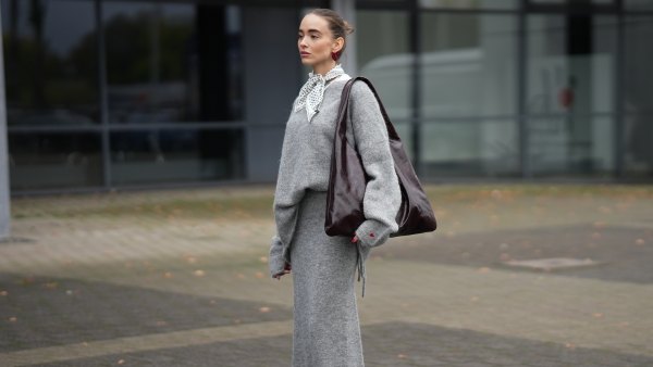 DUESSELDORF, GERMANY - OCTOBER 14: Evi Wave is seen wearing an oversized boatneck grey pullover by Aylin Koenig x Anita Hass with a slouchy fit, dropped shoulders and elongated sleeves made of a soft alpaca mix, it features an embroidered red heart one cuff; a full-length tube grey skirt by Aylin Koenig x Anita Hass in matching soft alpaca mix, with straight silhouette with a slightly flared hemline forming a co-ord set with the top; under the top she layered a white crewneck t-shirt; she carries an oversized shoulder hobo bag by Arket in high-shine patent leather in burgundy with a slouchy body; a pair of pointed-toe beige slingback kitten heels in monogram canvas by Gucci, featuring a brown logo-jacquard pattern, the GG motif with a low stiletto heel and brown leather piping around the edges, these worn with white ankle socks; on her fingers she wears silver rings from Ariane Ernst and Fossil; her nails are polished in red; she wears a silk carré Fraas scarf with a polka-dot print in monochrome black and white tones, tied in a classic French knot at the collar; she wears a pair of sculptural beaded earrings handmade with red glass beads by Kroon02; her brown hair is styled in a sleek, low bun on October 14, 2025 in Duesseldorf, Germany. (Photo by Moritz Scholz/Getty Images)