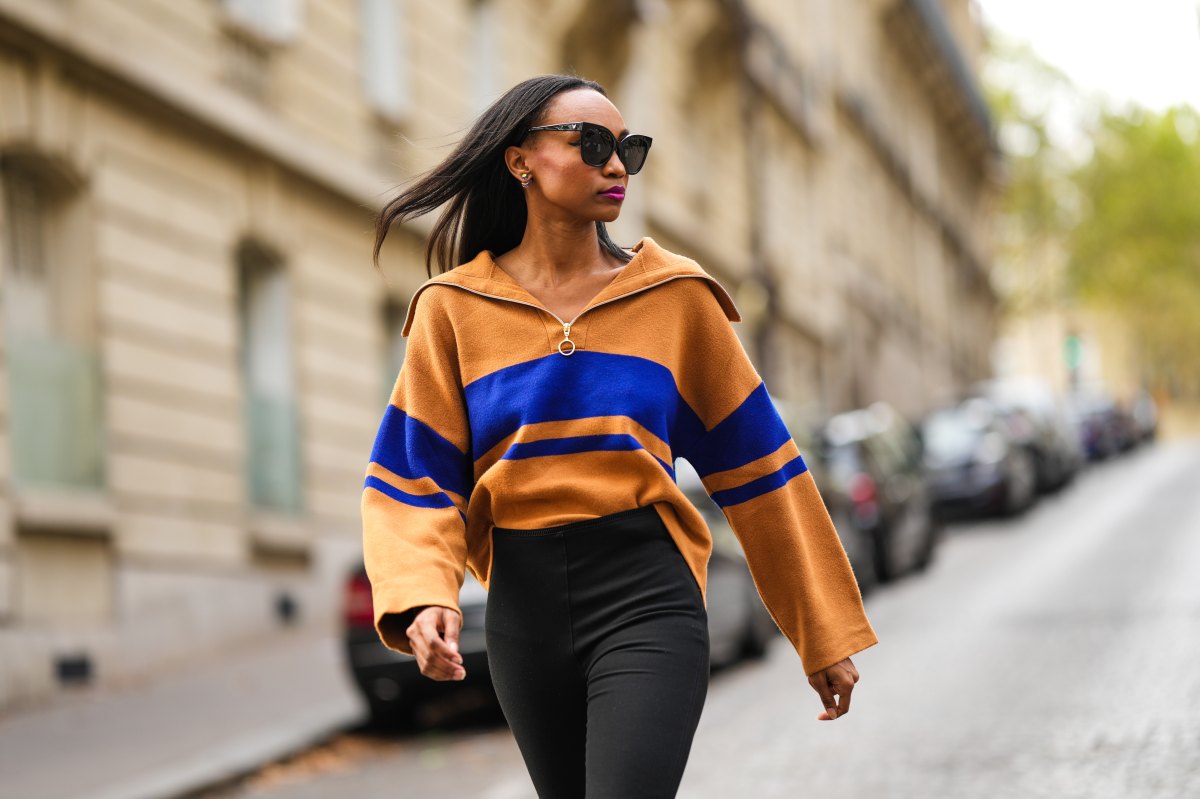 Emilie Joseph @in_fashionwetrust wears black sunglasses, silver and gold earrings, a half zipped wool blend sweater color blocked in tones of mustard and electric blue, black stirrup / slit leggings pants, during a street style fashion photo session, on September 19, 2021 in Paris, France.