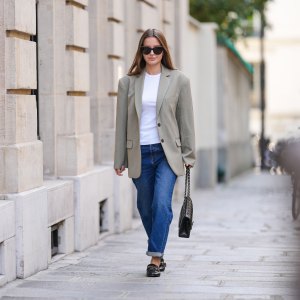 Diane Batoukina @diaanebt wears black sunglasses from Chanel, a white t-shirt, a beige gray oversized blazer jacket from Anine Bing, navy blue denim rolled-up large pants from Rouje, a black shiny grained leather Timeless handbag from Chanel, black shiny leather loafers mules from Massimo Dutti, during a street style fashion photo session, on April 15, 2022 in Paris, France.