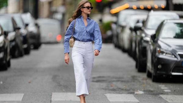Segolene Hyppolite wears sunglasses, a blue and white oversized shirt from Tommy Hilfiger, a raffia beige bag from Vanessa Bruno, high waist white denim pants from Vanessa Bruno, Chanel slingback shoes in blue denim with black tips, during a street style fashion photo session, on May 20, 2024 in Paris, France.