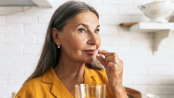 Cute mature female holding drugs and glass of water in hands. Elderly woman taking medication. Treatment course or vitamins complex idea. Healthy lifestyle and healthcare concept