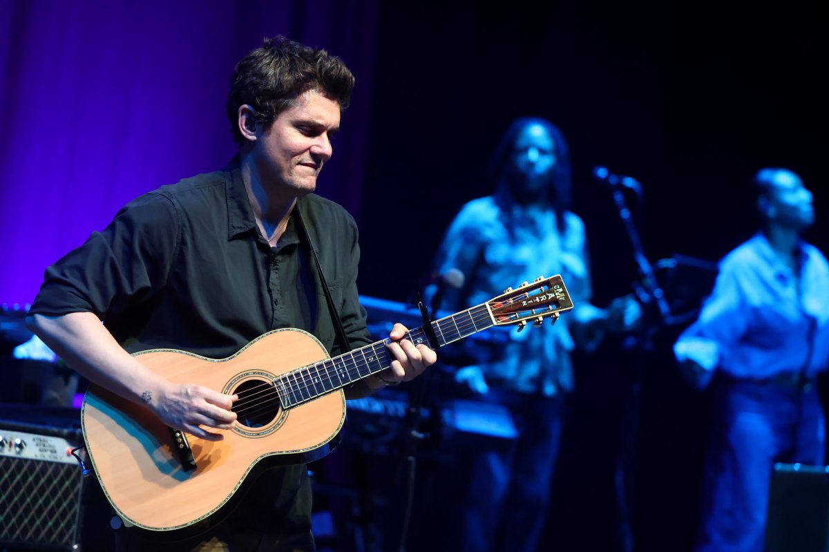 John Mayer playing an acoustic guitar while performing on stage.