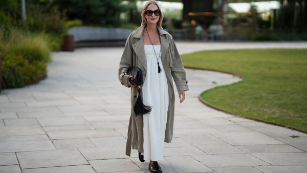 Louisa Theresa Grass wears oversized round sunglasses, a long taupe trench coat over a white strapless maxi dress, a long black tassel necklace, carries a black woven clutch with an oversized tassel and wears black loafers outside the Collina Strada show during day 4 of Copenhagen Fashion Week Spring Summer 2027 on August 6, 2026 in Copenhagen, Denmark.
