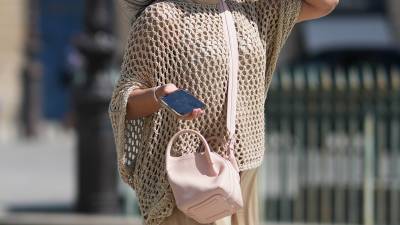 A passerby wears a biege knit fishnet mesh oversized top with wide sleeves, a pale pastel pink leather shoulder crossbody bag, during a street style fashion photo session, on August 22, 2026 in Paris, France.