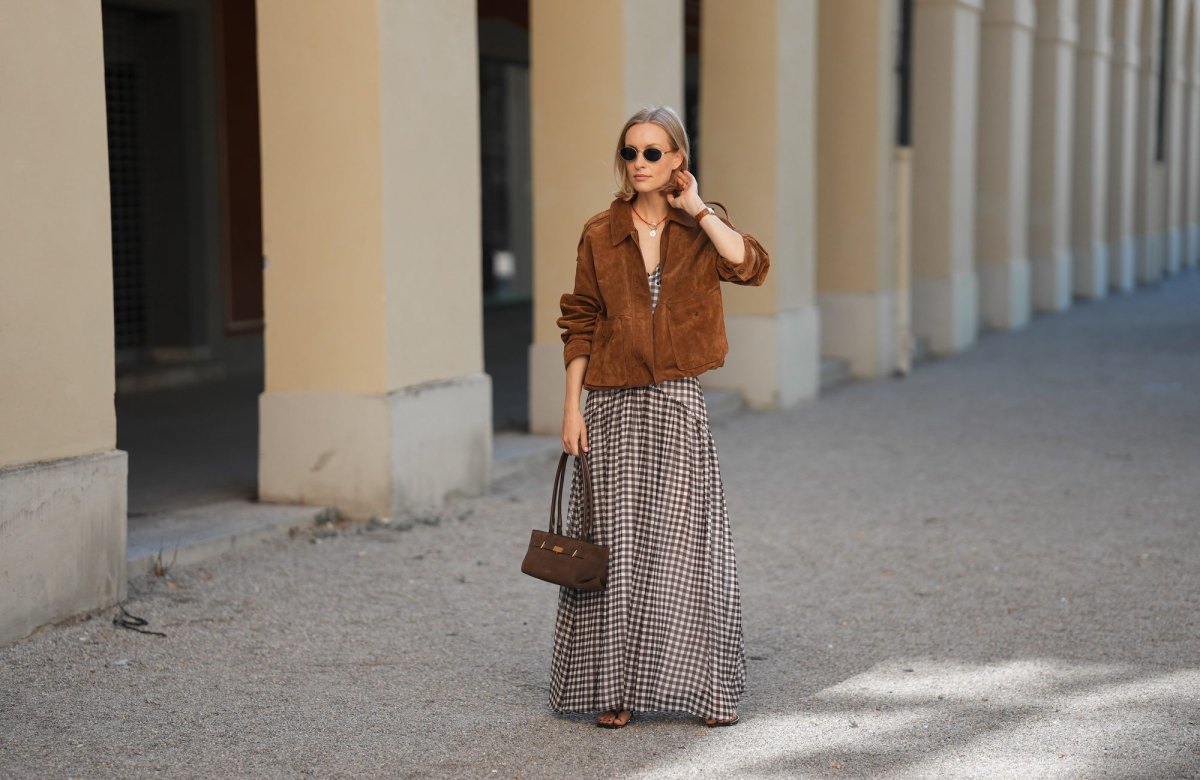 MUNICH, GERMANY - JULY 18: Marlies Pia Pfeifhofer is seen wearing a dark camel brown suede bomber jacket with flap pockets, elasticized cuffs and hem and a front zipper closure from Zara; a brown and white Toulouse gingham check maxi dress with a V-neckline, a high front slit, an A-shaped hip cut and a pleated skirt from ADOORE; a dark brown suede The New York shoulderbag with top handles, triangular fold design and golden hardware from DeMellier; chocolate brown flip flop sandals with wide thong straps and kitten heel from H&M; round sunglasses with golden temples and dark lenses from Persol; a surigao pearl necklace with red Japanese glass beads and a freshwater baroque pearl from Les Beads Studio; a golden medallion necklace with faceted diamond bezel and hand-painted 'Porte Bonheur' enamel from Marlo Laz; small golden hoop earrings from Monica Vinader; a vintage square Tank wristwatch with light brown leather strap from Cartier; her blonde hair is styled in a straight bob with a center part on July 18, 2025 in Munich, Germany. (Photo by Moritz Scholz/Getty Images)