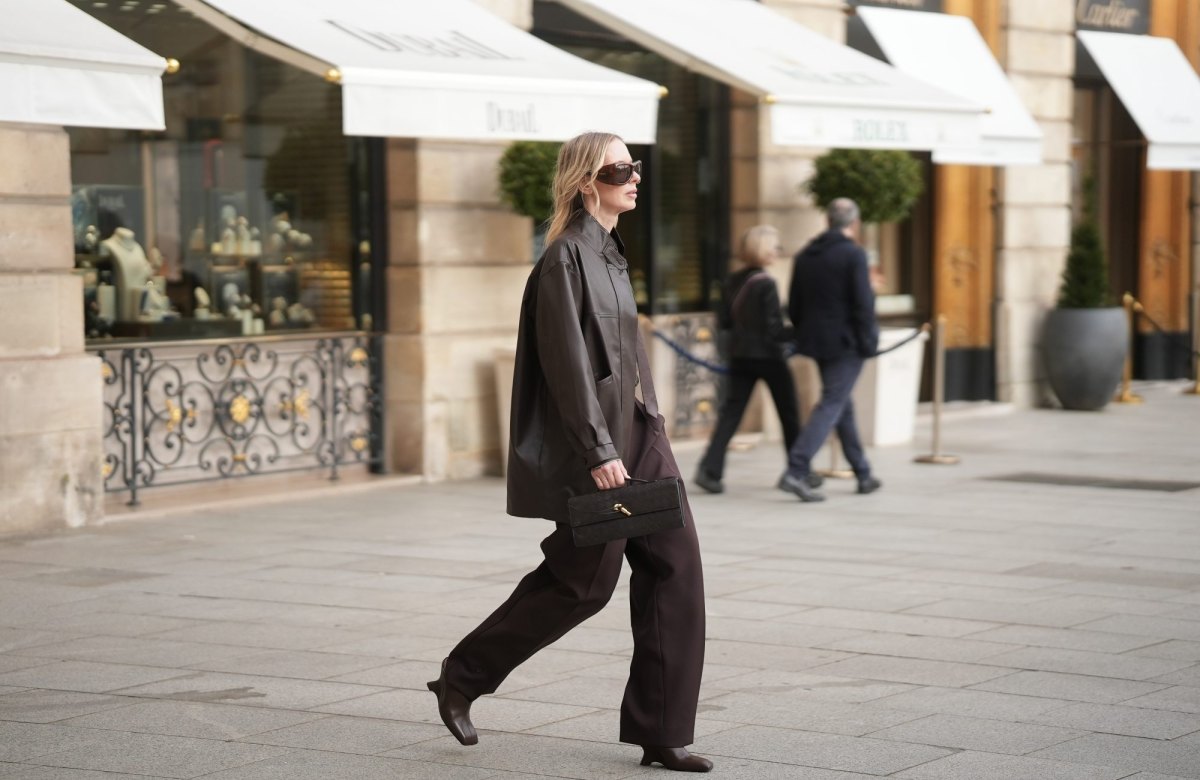 PARIS, FRANCE - MARCH 5: Mirja Klein is seen wearing a dark brown leather jacket with a relaxed oversized silhouette, stand collar collar and front button closure from The Frankie Shop; a brown and white striped shirt with a pointed collar from The Frankie Shop; a brown tie from The Frankie Shop; high waisted dark brown "Doyer" pleated pants with a straight leg silhouette from The Frankie Shop; dark brown leather "The Polka pebble leather pump" with a square toe and sculptural heel from Rodjber; she carries a brown intrecciato "Andiamo" leather clutch bag with a signature gold knot element from Bottega Veneta; oversized brown sunglasses with a thick acetate frame from Saint Laurent; her blonde hair is worn loose in soft waves with a center part during Day Four of Paris Fashion Week - Womenswear Fall/Winter 2026/2027 on March 5, 2026 in Paris, France. (Photo by Moritz Scholz/Getty Images)