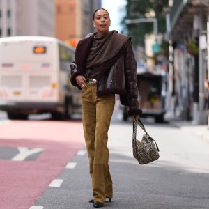 NEW YORK, NEW YORK - SEPTEMBER 12: Olivia Galli wears dark brown slicked back hair in a low bun, a burgundy shearling leather jacket, a brown wool draped cowl-neck top, a suede camel straight-leg pants, a wide tan belt with an oval silver buckle, a beige tote bag with black leopard print and double top handles, black pointed-toe high heels ankle boots shoes, outside Altuzarra, during New York Fashion Week, on September 12, 2026 in New York, New York (Photo by Edward Berthelot/Getty Images)