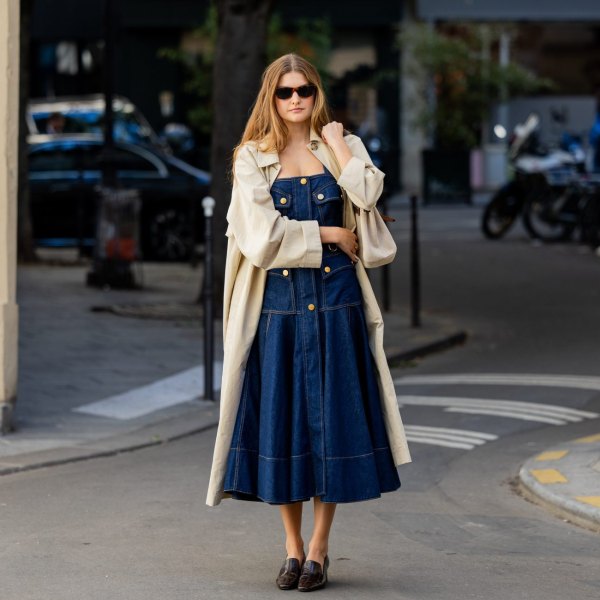 PARIS, FRANCE - OCTOBER 05: Sara Walker wears a dark wash denim midi dress with brass button details, a light beige trench coat, dark brown sunglasses and black patent leather block heel loafers outside Zimmermann on October 05, 2026 in Paris, France. (Photo by Christian Vierig/Getty Images)