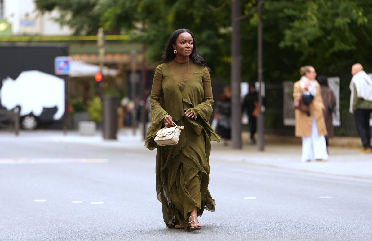 PARIS, FRANCE - OCTOBER 06: A guest wears long straight black hair past the shoulders with a center part, gold hoop earrings, a beige quilted leather shoulder bag with a gold chain strap, an olive green chiffon long-sleeve ruffled maxi dress with a sheer yoke and horizontal sheer paneling, tiered ruffle skirt, fluted bell sleeves and a front high slit, metallic gold strappy sandals shoes with thin stiletto heels, outside Zimmermann, during Paris Fashion Week - Womenswear Spring Summer 2026, on October 06, 2025 in Paris, France (Photo by Edward Berthelot/Getty Images)