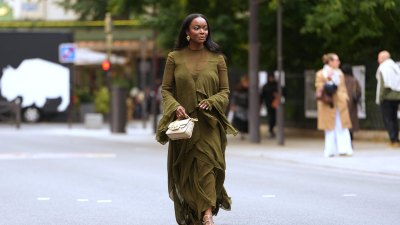 PARIS, FRANCE - OCTOBER 06: A guest wears long straight black hair past the shoulders with a center part, gold hoop earrings, a beige quilted leather shoulder bag with a gold chain strap, an olive green chiffon long-sleeve ruffled maxi dress with a sheer yoke and horizontal sheer paneling, tiered ruffle skirt, fluted bell sleeves and a front high slit, metallic gold strappy sandals shoes with thin stiletto heels, outside Zimmermann, during Paris Fashion Week - Womenswear Spring Summer 2026, on October 06, 2025 in Paris, France (Photo by Edward Berthelot/Getty Images)