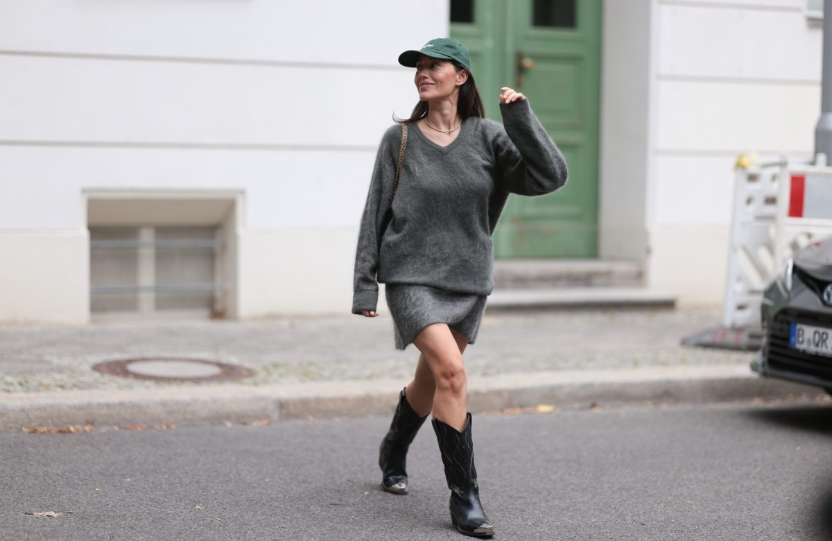 BERLIN, GERMANY - SEPTEMBER 16: Anna Schürrle seen wearing dark green Fulfilled baseball cap with white embroidered lettering at the front. Her hair is straight and left down, tucked behind her ears so the cap frames her face neatly. Her makeup is minimal and natural. Around her neck, she has a delicate gold tennis necklace, Soft Goat cozy oversized v-neck sweater in a soft, fuzzy grey knit. The relaxed fit, with slightly long sleeves, creates an effortless, slouchy silhouette, matching Soft Goat mini skirt, also in fuzzy grey knit. The skirt features an asymmetrical hemline, Chanel black 2.55 handbag, worn on the shoulder with the signature gold chain strap and Dorothee Schumacher cowboy boots in black leather. The boots feature detailed stitching along the shaft and silver metallic tips at the toes, on September 16, 2025 in Berlin, Germany. (Photo by Jeremy Moeller/Getty Images)