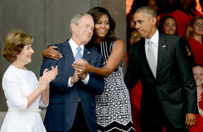 Barack Obama watches Michelle Obama embracing former president George Bush, accompanied by his wife, former first lady Laura Bush, while participating in the dedication of the National Museum of African American History and Culture September 24, 2016 in Washington, DC.