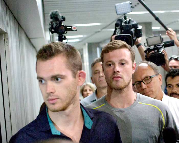 Journalists surround American Olympic swimmers Gunnar Bentz, left, and Jack Conger, center, as they leave the police station at Rio International airport early Thursday Aug. 18, 2016.