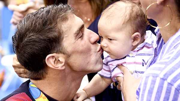 USA's Michael Phelps (L) kisses his son Boomer next to his partner Nicole Johnson (R) and mother Deborah (C) after he won the Men's 200m Butterfly Final during the swimming event at the Rio 2016 Olympic Games at the Olympic Aquatics Stadium in Rio de Janeiro on August 9, 2016.