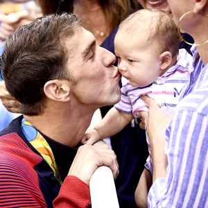 USA's Michael Phelps (L) kisses his son Boomer next to his partner Nicole Johnson (R) and mother Deborah (C) after he won the Men's 200m Butterfly Final during the swimming event at the Rio 2016 Olympic Games at the Olympic Aquatics Stadium in Rio de Janeiro on August 9, 2016.